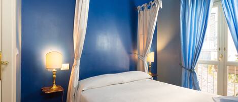Une chambre à coucher avec un lit, deux lampes de chevet, une fenêtre avec des rideaux et une pile de serviettes.