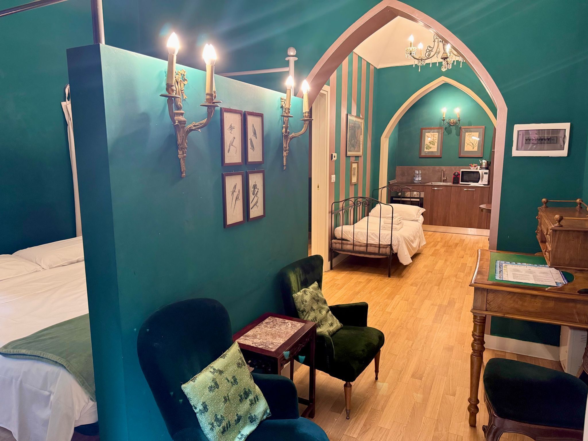 A room with teal walls, a bed, a desk, a chair, and a kitchenette.