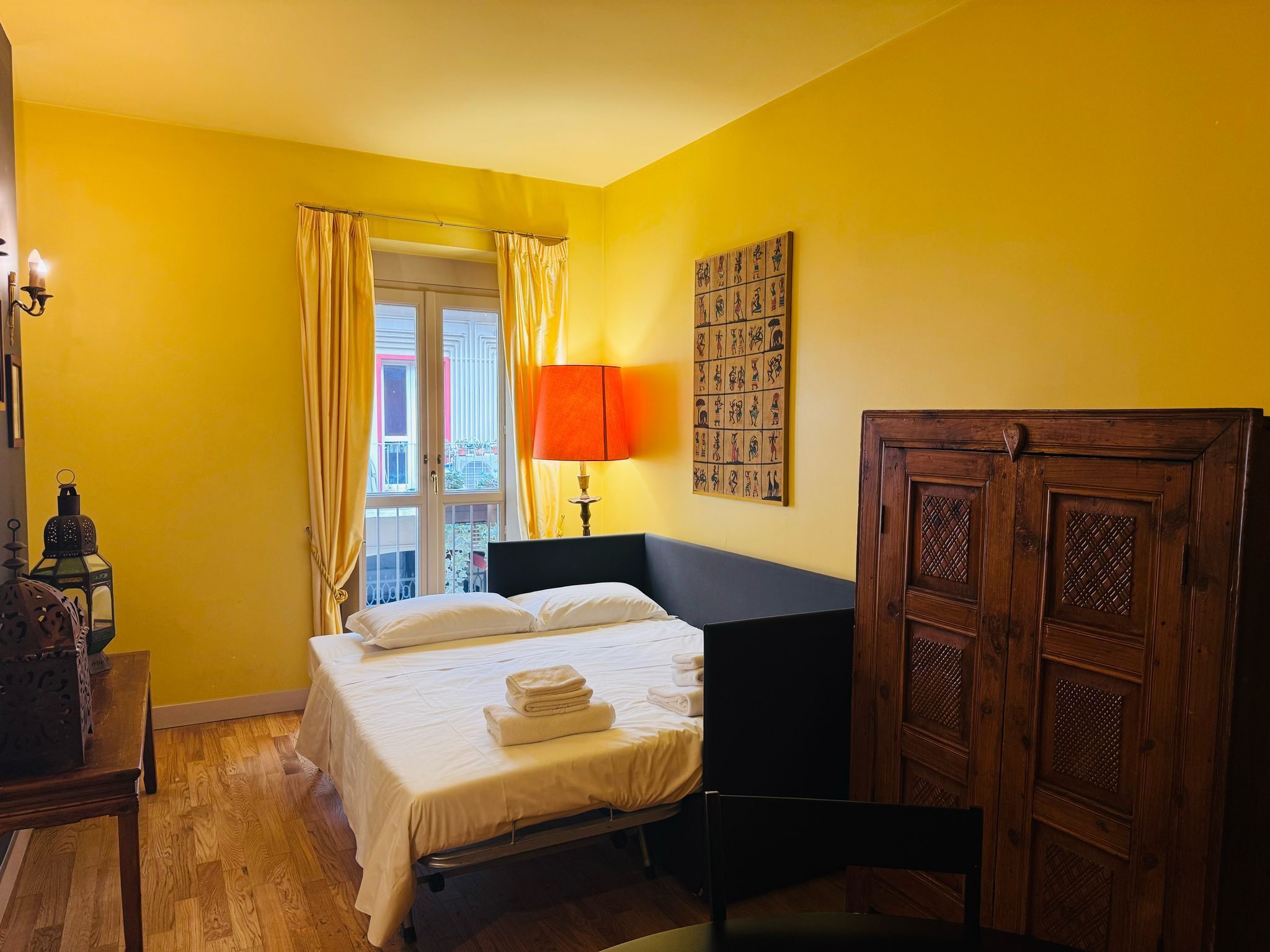 A room with a bed, a lamp, a wooden wardrobe, and a window with curtains.