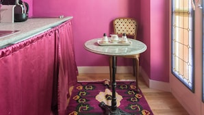 A pink-walled room with a round table, a chair, a radiator, and a window with a stained glass design. - Residence Porta Palace - Welkome Apartments (Turin)