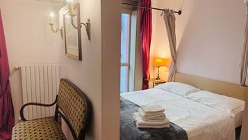 Una habitación de hotel con cama, una silla, un radiador, una lámpara y cortinas.