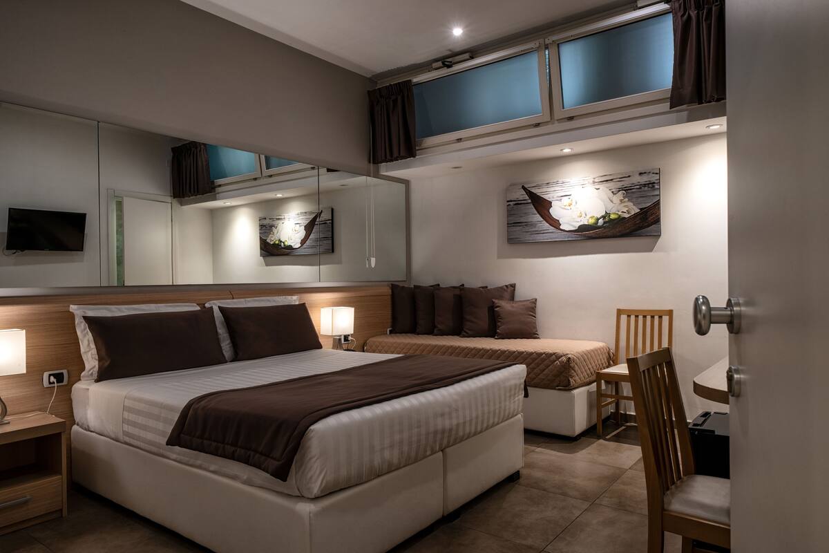 Une chambre d’hôtel moderne dotée d’un grand lit, d’un canapé-lit plus petit, d’un coin repas et d’une télévision.