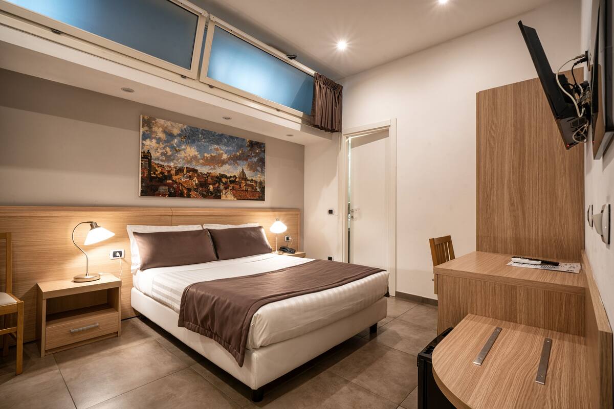 Une chambre d’hôtel moderne, équipée d’un lit, de tables de chevet, d’un bureau et d’un tableau au mur.