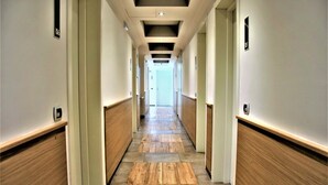 Een hotelgang met houten lambrisering, een betegelde vloer en deuren aan beide kanten die naar kamers leiden.