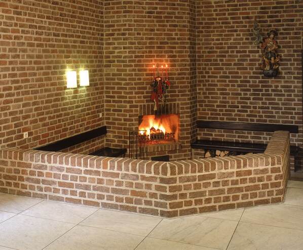 A brick fireplace with a fire, a bench, and a statue on the wall. - Maternushaus (Cologne)