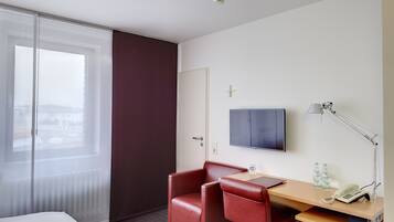 Una habitación de hotel con una cama, un escritorio con lámpara, un televisor y una silla roja.