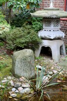 Un farol de piedra en un jardín con un estanque, rodeado de rocas y follaje.