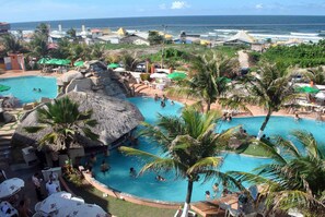 A resort with a large central pool surrounded by palm trees and thatched-roof structures. - Hotel Privê do Atalaia (Salinópolis)