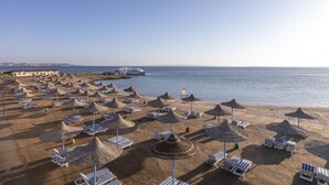 Ein Strand mit Reihen von Liegestühlen und Reetsonnenstühlen, ein Pier im Hintergrund und ein ruhiges Meer.