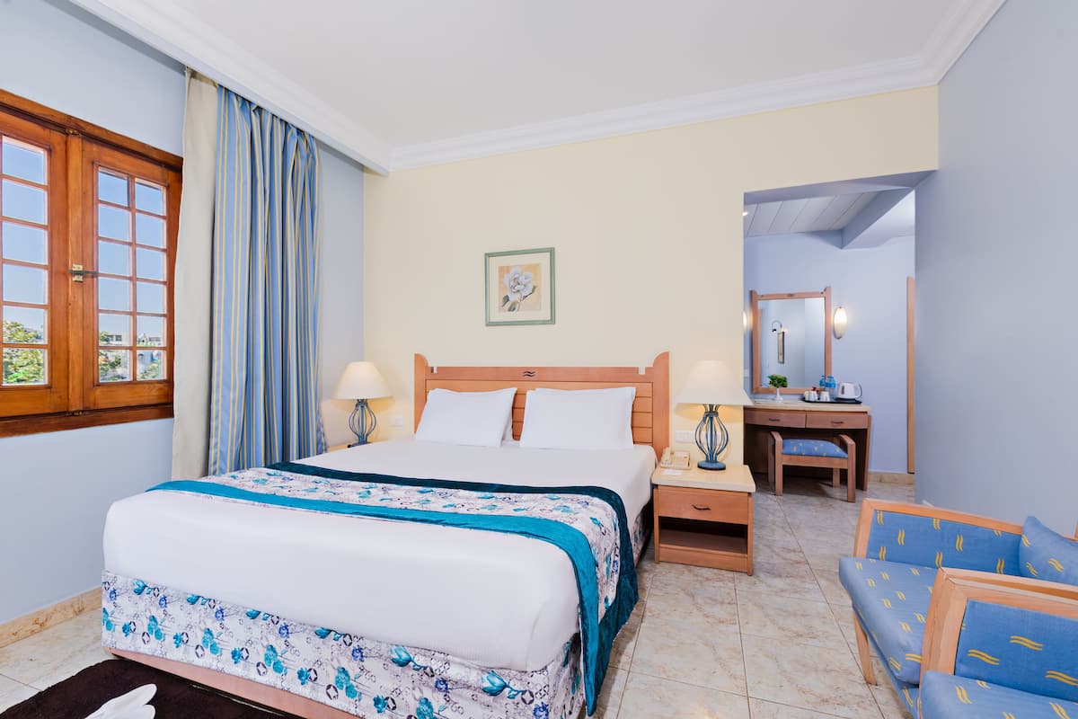 Una habitación de hotel con una cama, mesitas de noche, un escritorio, una silla y un espejo.