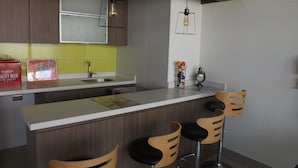 A modern kitchen with wooden cabinets, a white countertop, and a bar area with three stools. - Edificio Vive Viana I (Vina del Mar)