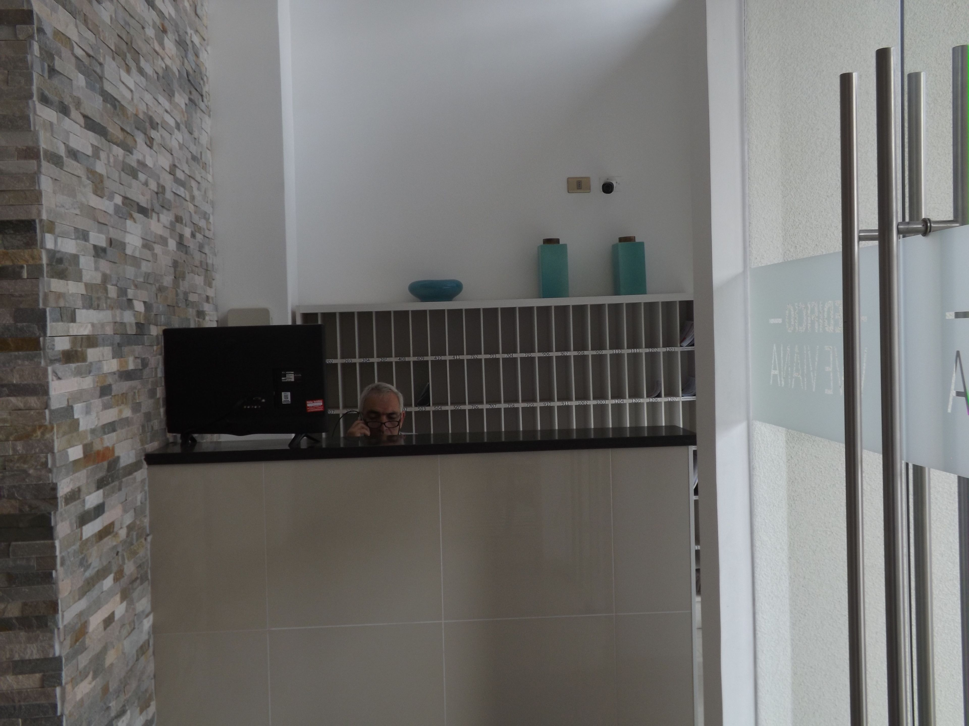 A bathroom with a tiled wall, a black countertop, and a glass door with a sign.