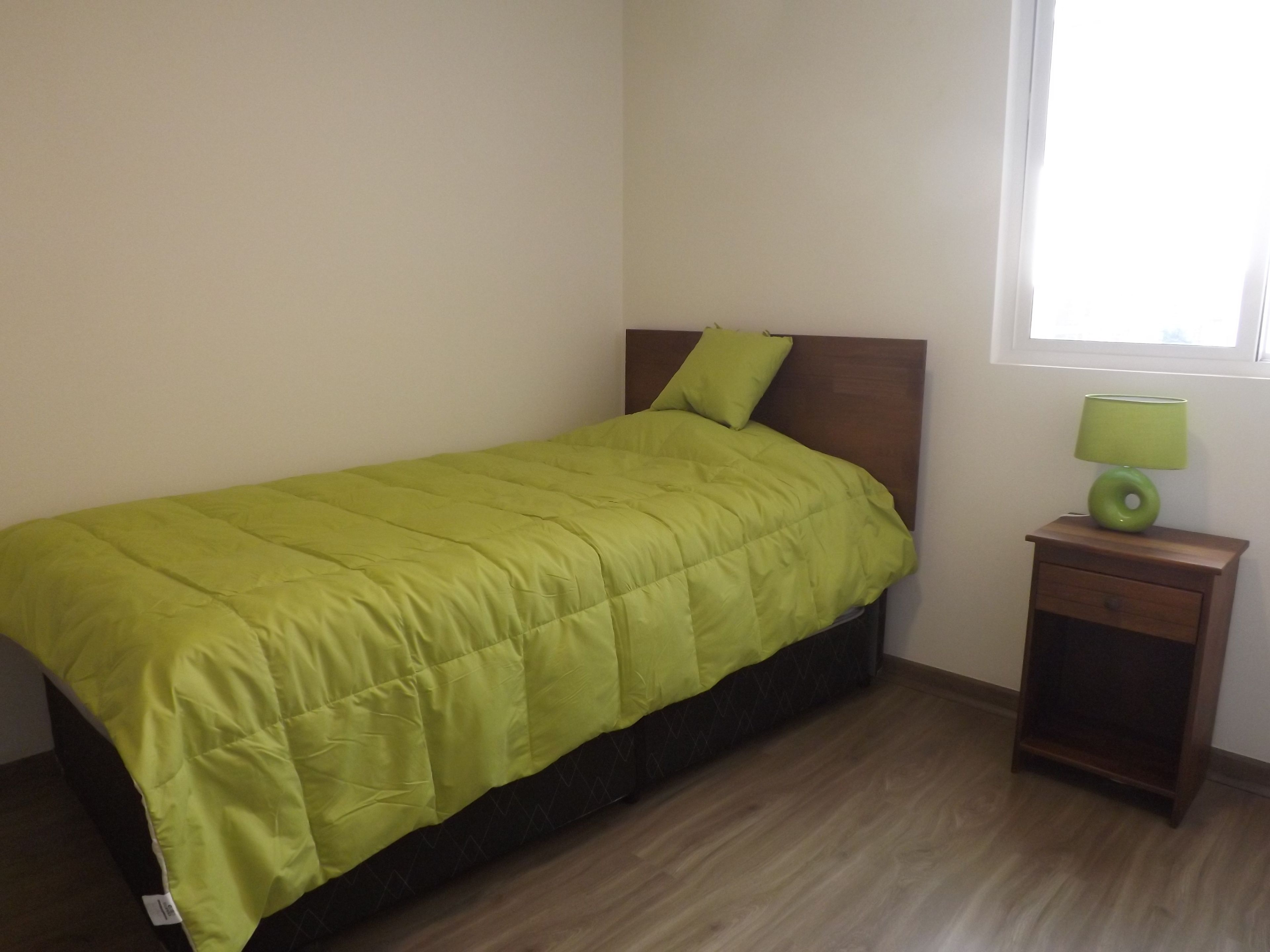 A bedroom with a bed, a nightstand, a lamp, and a window.