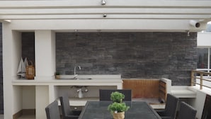 A modern kitchen with a stone backsplash, a built-in sink, and a dining area with wicker chairs and a small potted plant. - Edificio Vive Viana I (Vina del Mar)