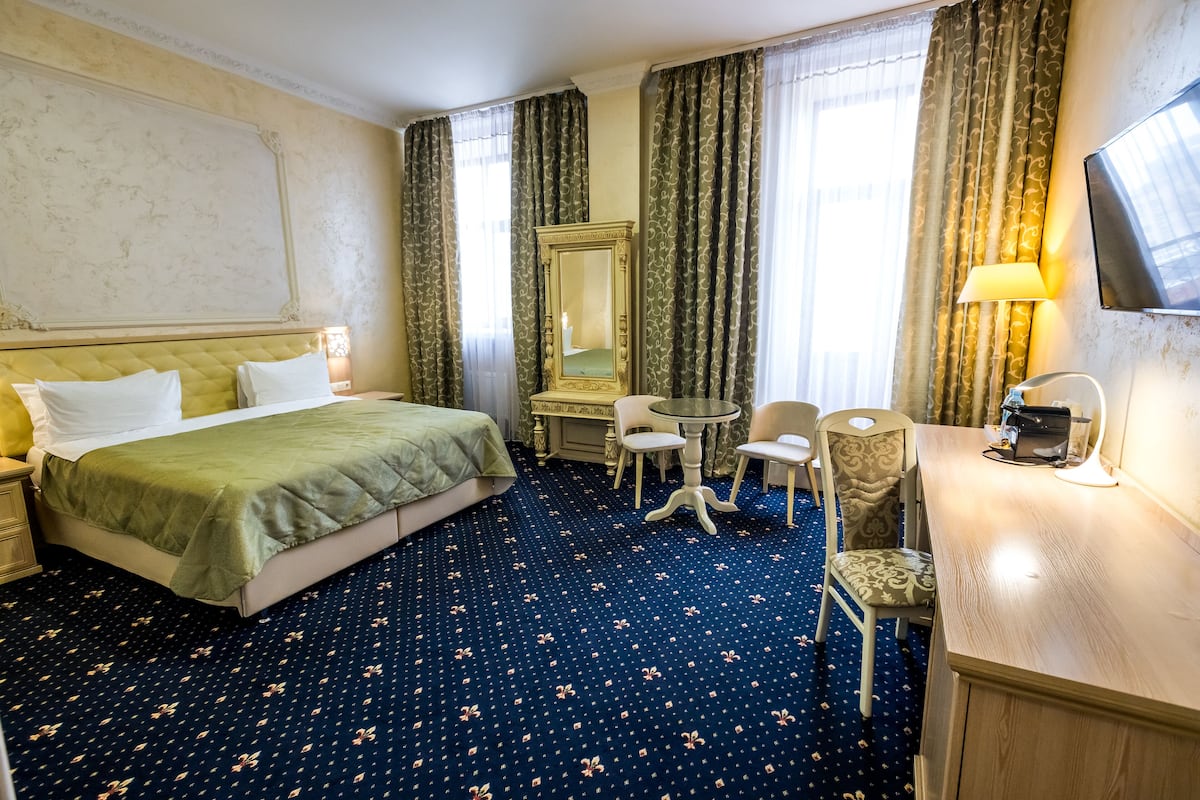 A hotel room with a bed, a desk, a chair, a table, a mirror, and a television.