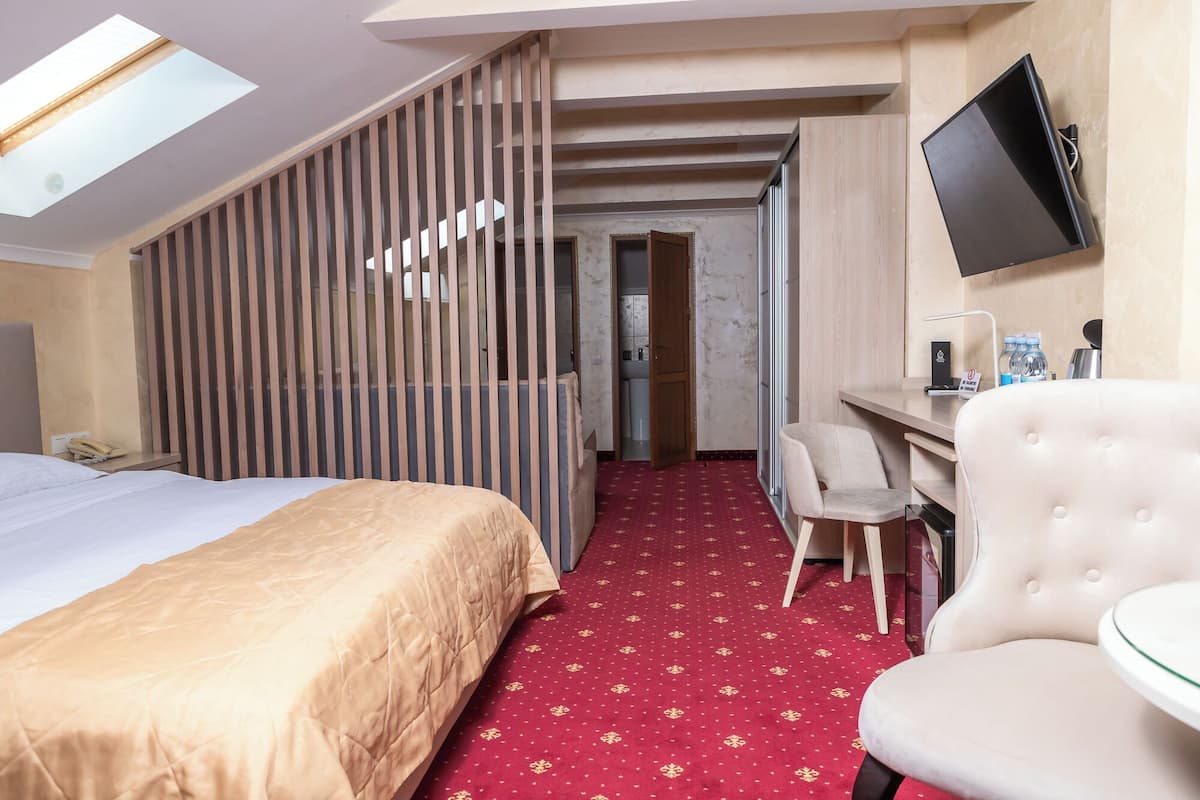 A hotel room with a bed, a desk, a chair, a TV, and a red carpet.
