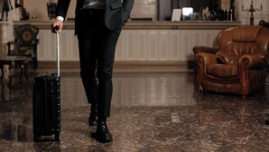 A person in a suit pulling a suitcase in a room with a marble floor, a leather armchair, and a wooden cabinet. - Hotel France (Vinnytsia)