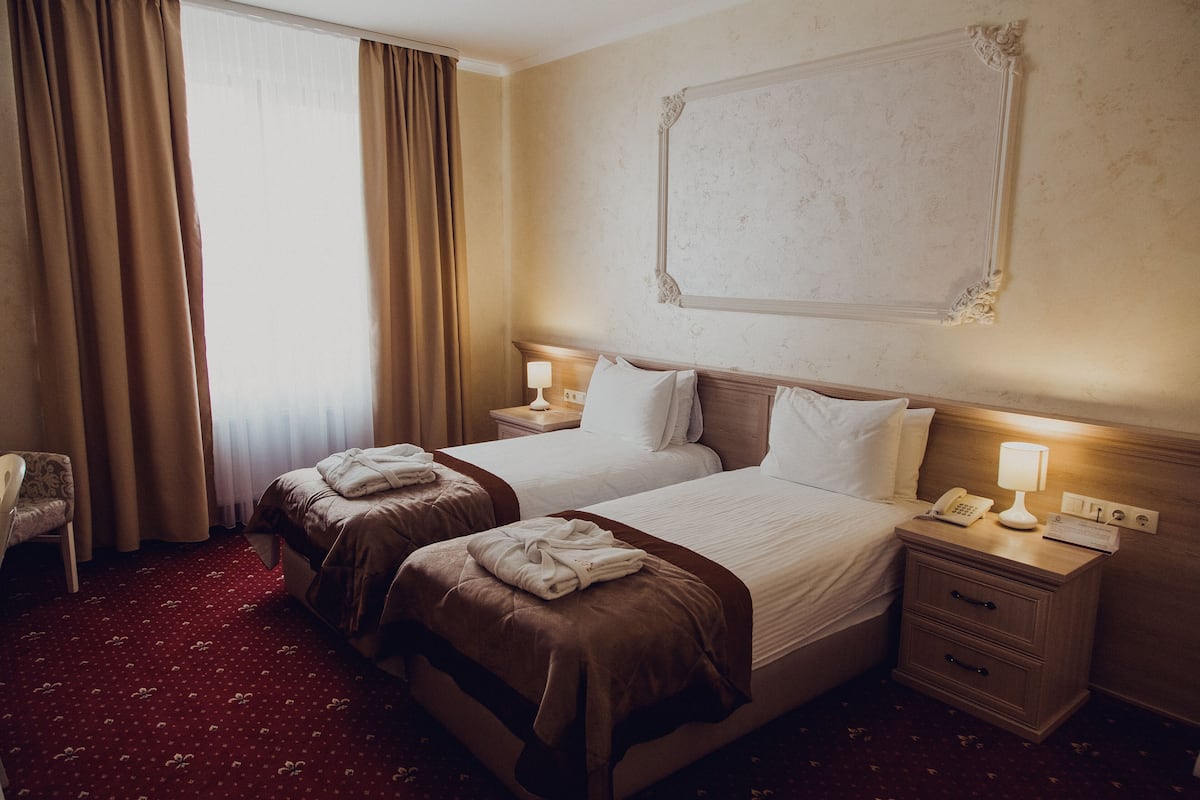 A hotel room with two beds, a nightstand with a lamp, a chair, and a large mirror on the wall.