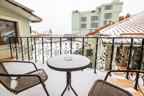 A balcony with a round table and two wicker chairs, a metal railing, and buildings in the background.