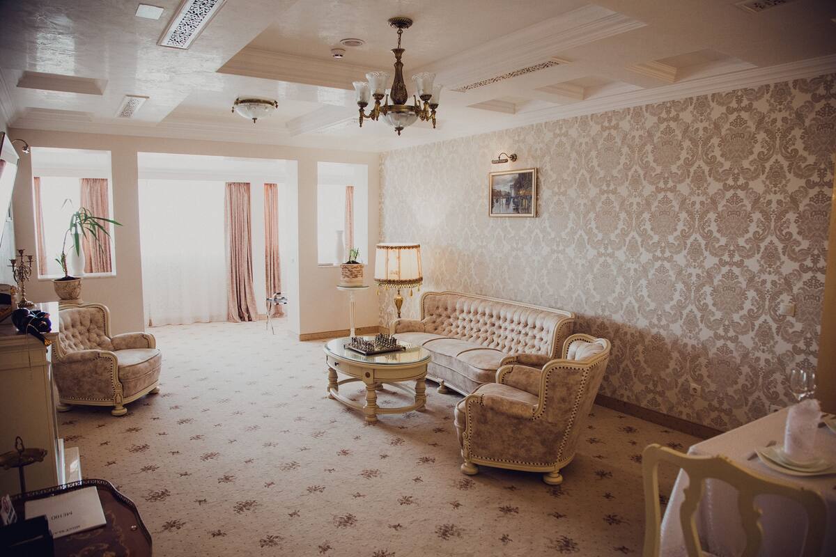 A spacious living room with a chandelier, a sofa, armchairs, a coffee table, and a dining table with a vase.