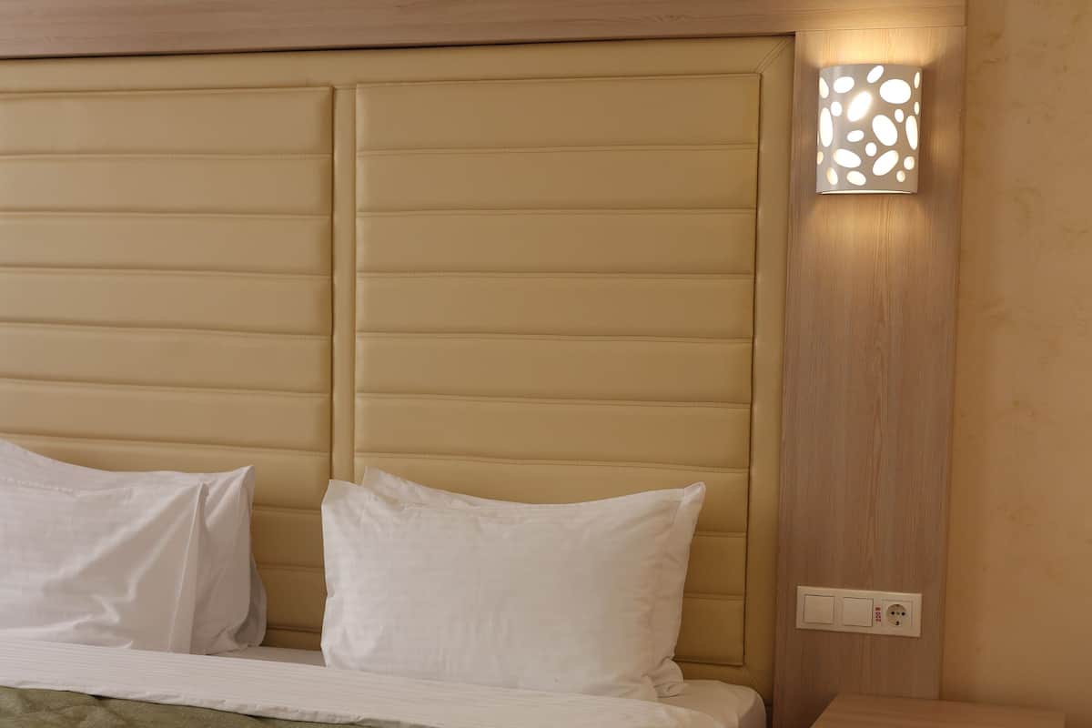 A neatly made bed with a green blanket, a wooden headboard, and a bedside table with a drawer.