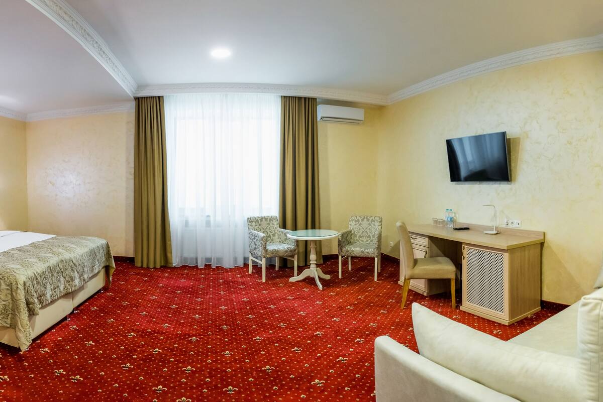 A hotel room with a large bed, a desk with a chair, a small table with two chairs, and a TV mounted on the wall.