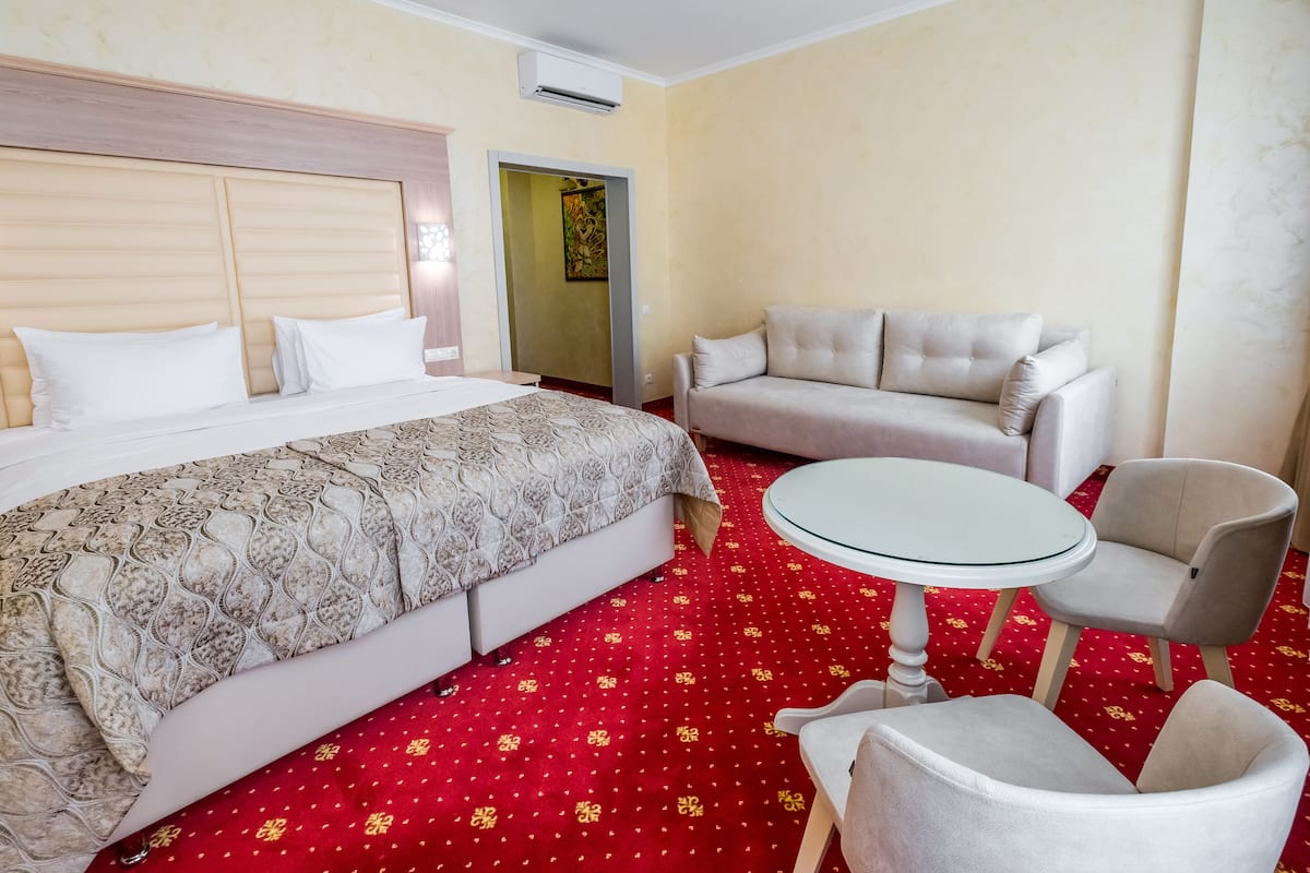 A hotel room with a bed, a sofa, a round table, and a red carpet.