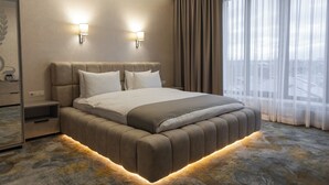 A modern hotel room with a large bed, two bedside lamps, a nightstand, and a view of the city through sheer curtains. - Hotel France (Vinnytsia)