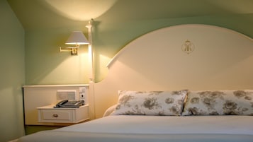 A hotel room with a bed, a nightstand with a telephone, and a wall-mounted lamp.