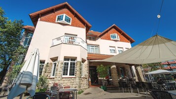 A two-story building with a stone facade, a balcony, and outdoor seating area with umbrellas.