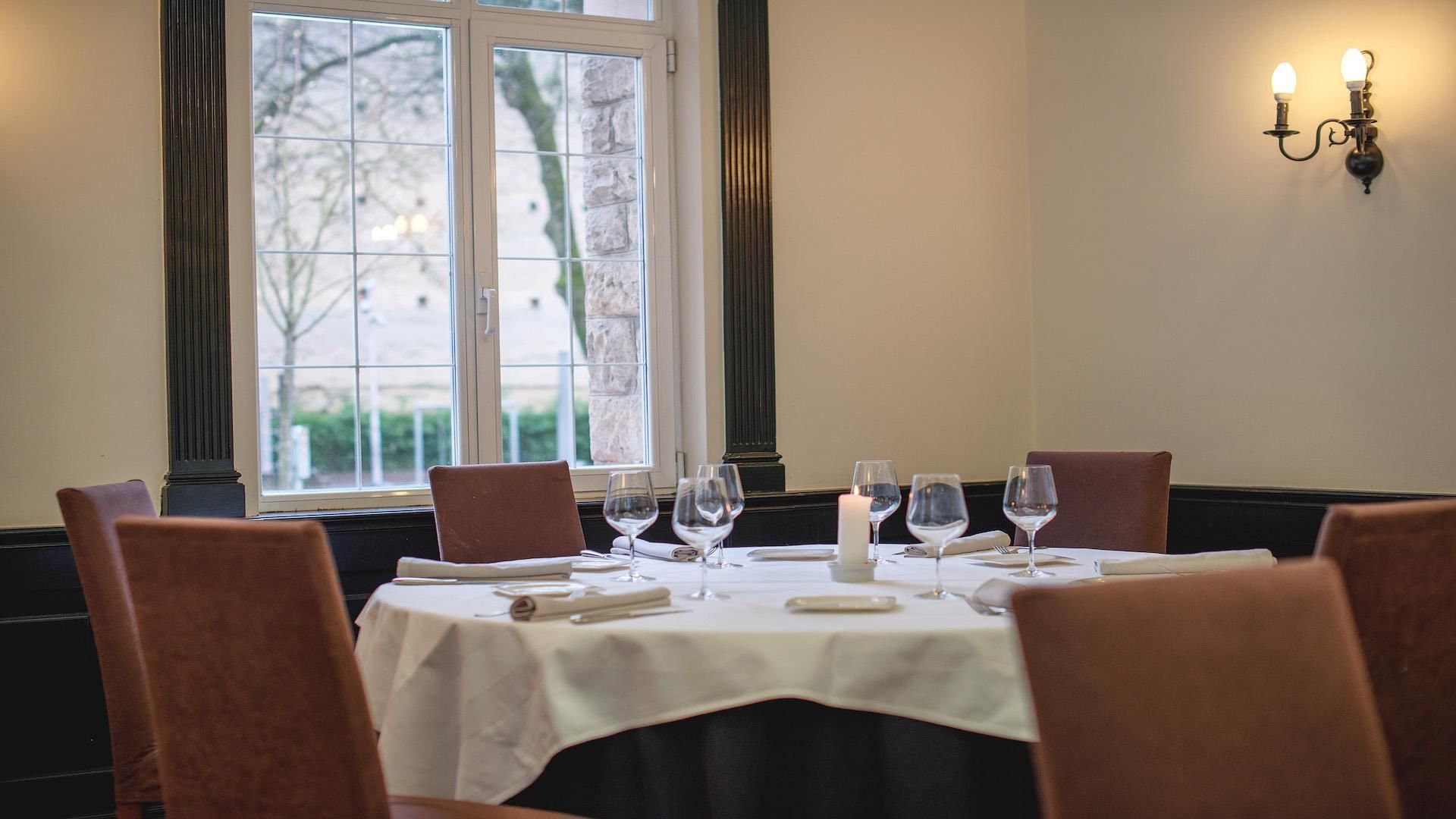 A dining table set for four with wine glasses, a candle, and a menu.