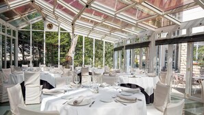 A conservatory with round tables set for dining, large windows, and a glass ceiling. - Hotel Harrison Etxea (Amorebieta)