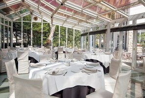 A conservatory with round tables set for dining, large windows, and a glass ceiling.