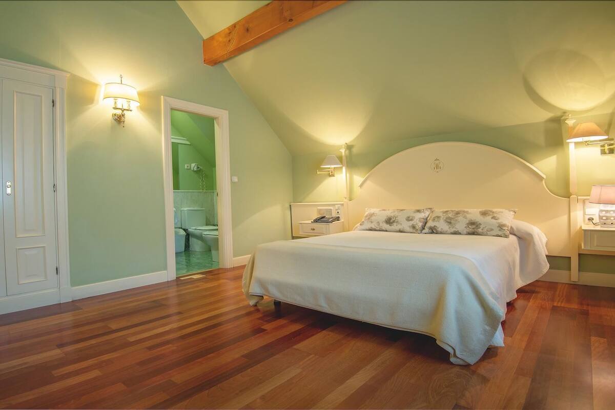 A bedroom with a sloped ceiling, a bed with floral bedding, two bedside lamps, and a wooden floor.