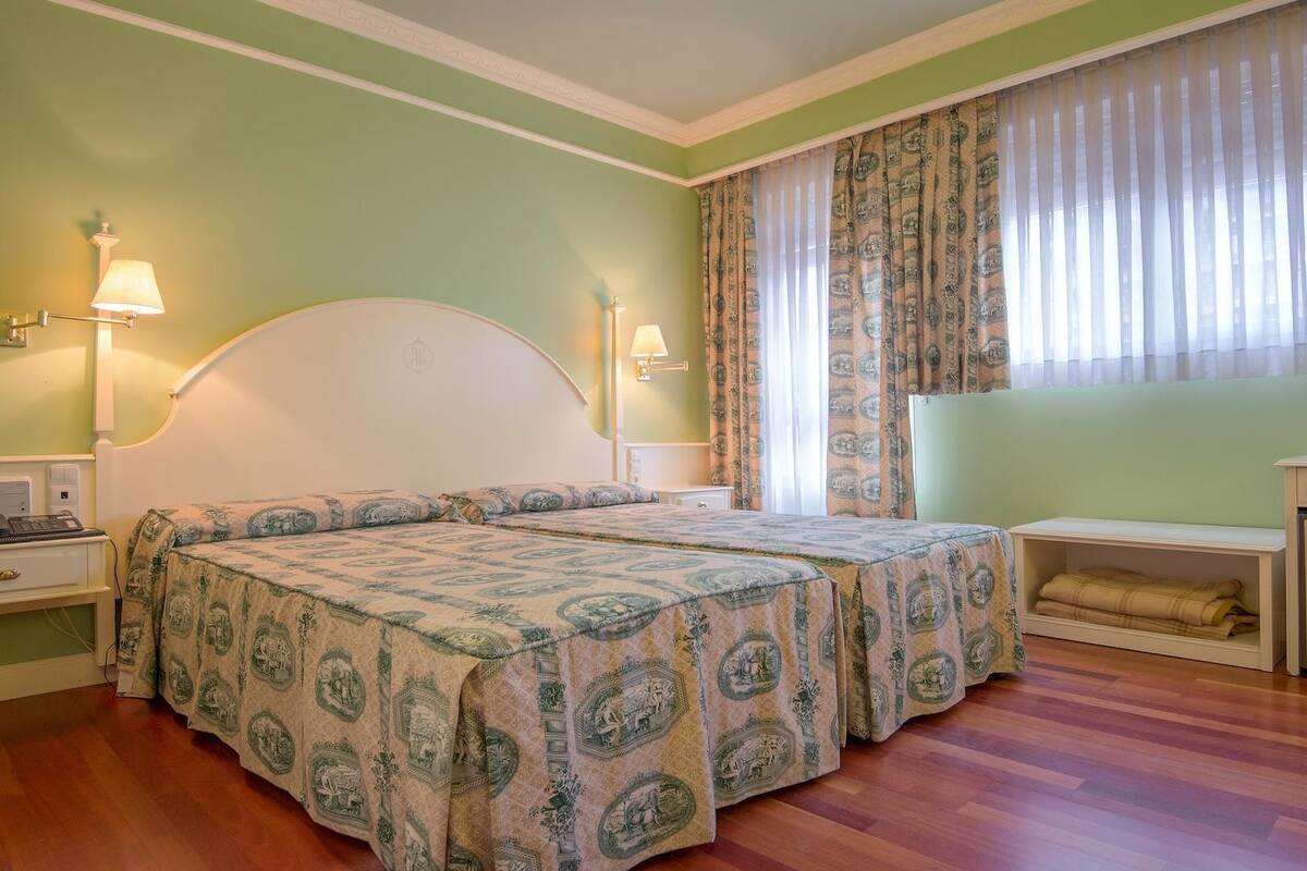 A hotel room with two beds, a nightstand with a lamp, a bedside table, and a wardrobe.