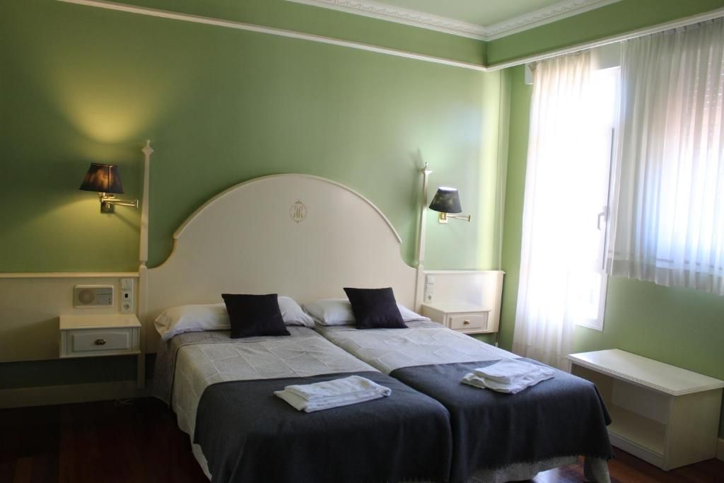 A double bed with two pillows, a bedside table, a lamp, and a window with curtains.