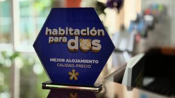 Un panneau hexagonal portant l’inscription « habitación para dos » et « MEJOR ALOGAMIENTO CALIDAD-PRECIO » sur une surface réfléchissante.