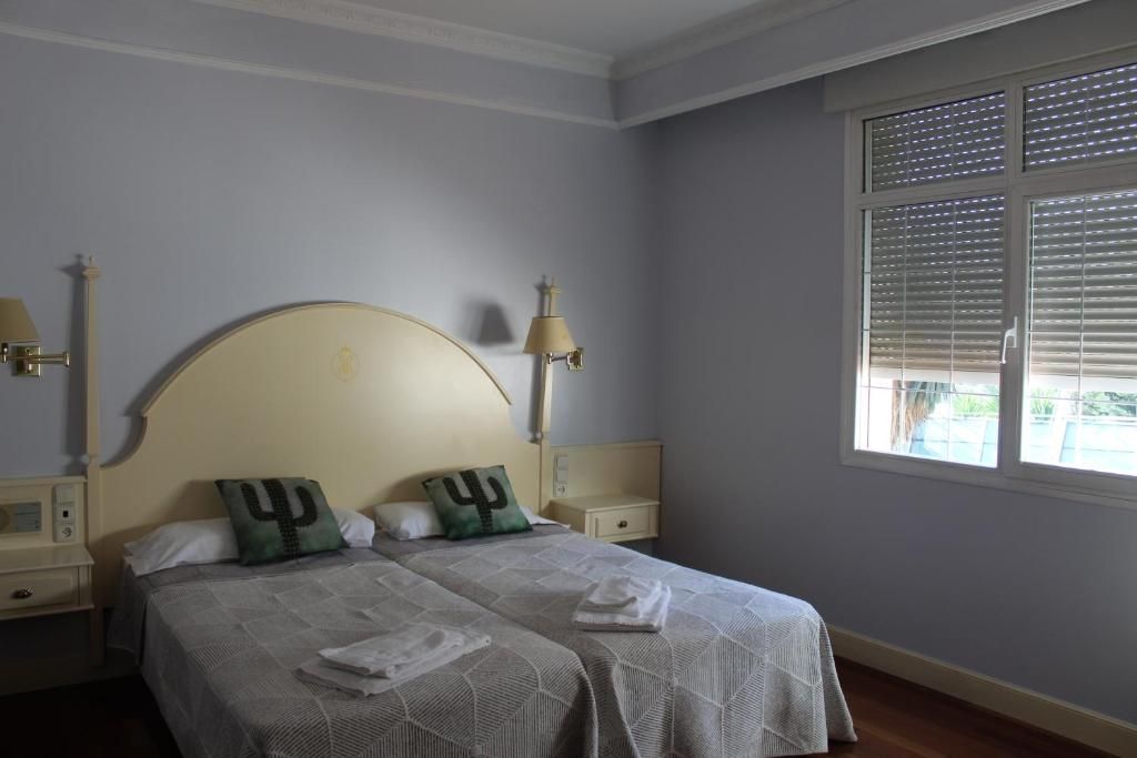 A bedroom with a double bed, two bedside tables, a lamp, and a window with blinds.