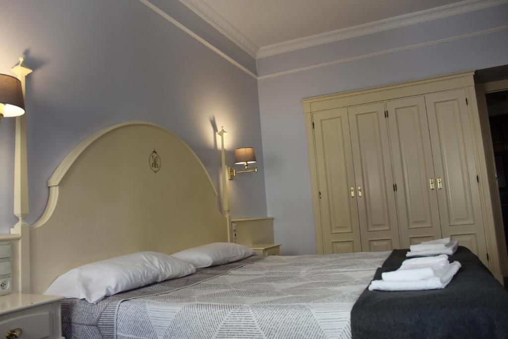 A bedroom with a large bed, bedside lamps, a wardrobe, and neatly folded towels.