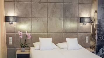 A modern hotel room with a large bed, two bedside tables, a vase with flowers, and a wall-mounted light fixture.