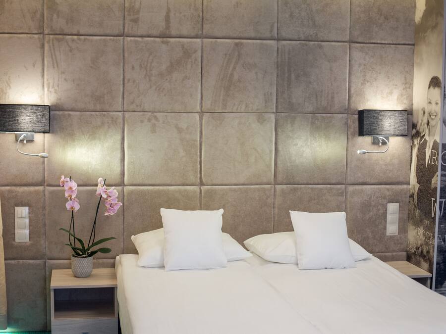 A modern hotel room with a large bed, two bedside tables, a vase with flowers, and a wall-mounted light fixture.