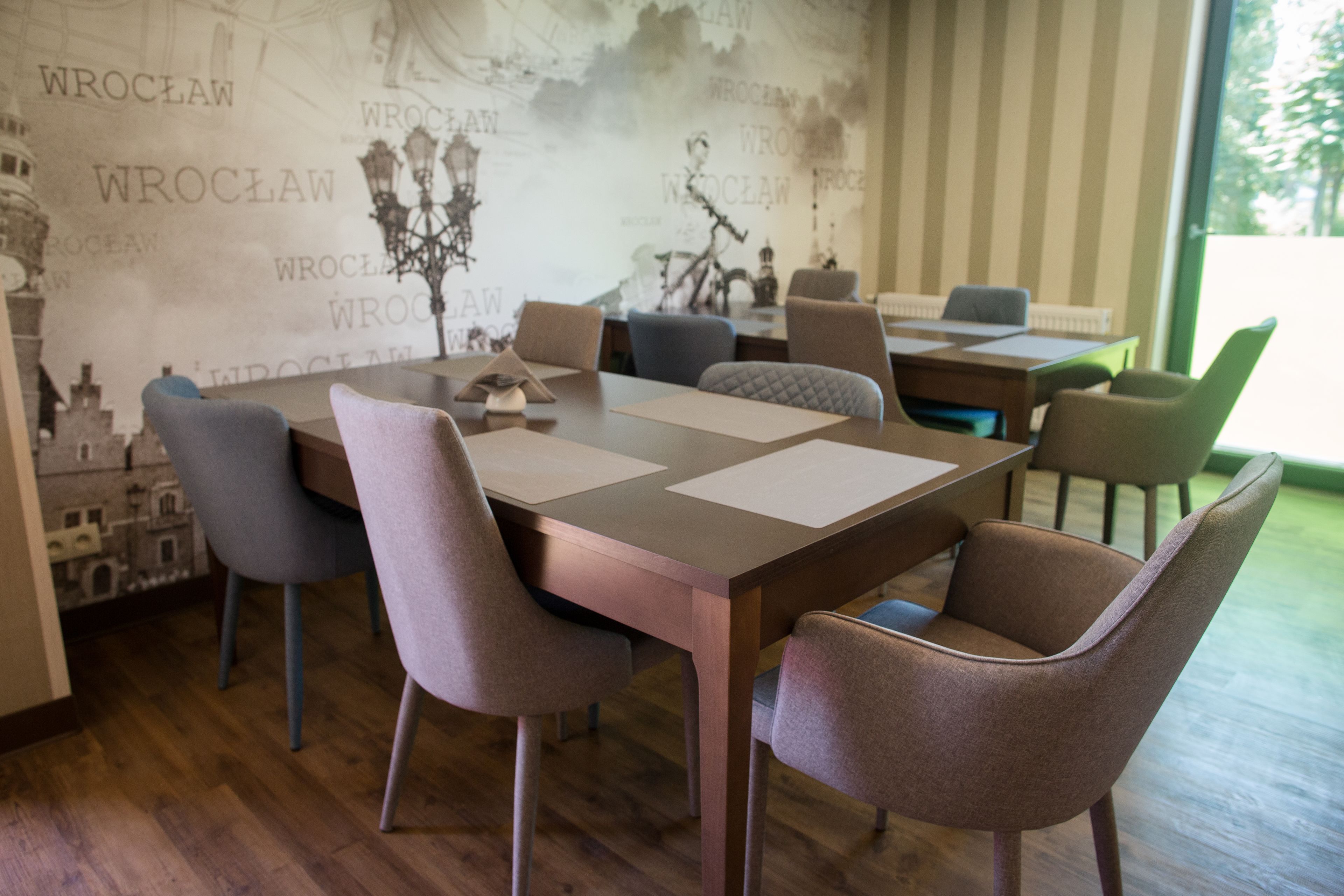 A dining area with a table set for four, surrounded by chairs. The room features a large window and a wall with a cityscape mural.