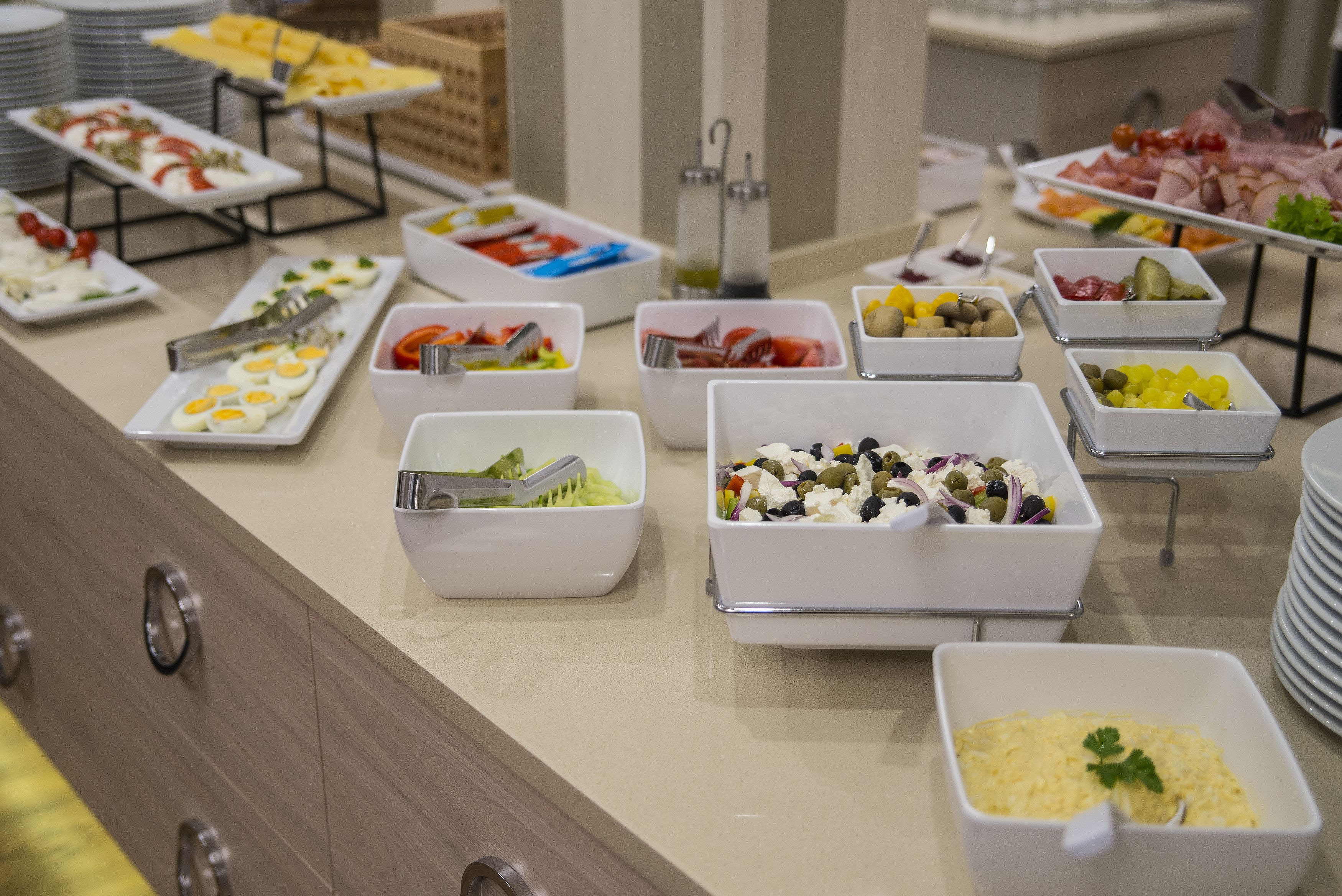 A buffet with various food items in white bowls and plates, including eggs, salads, and meats.