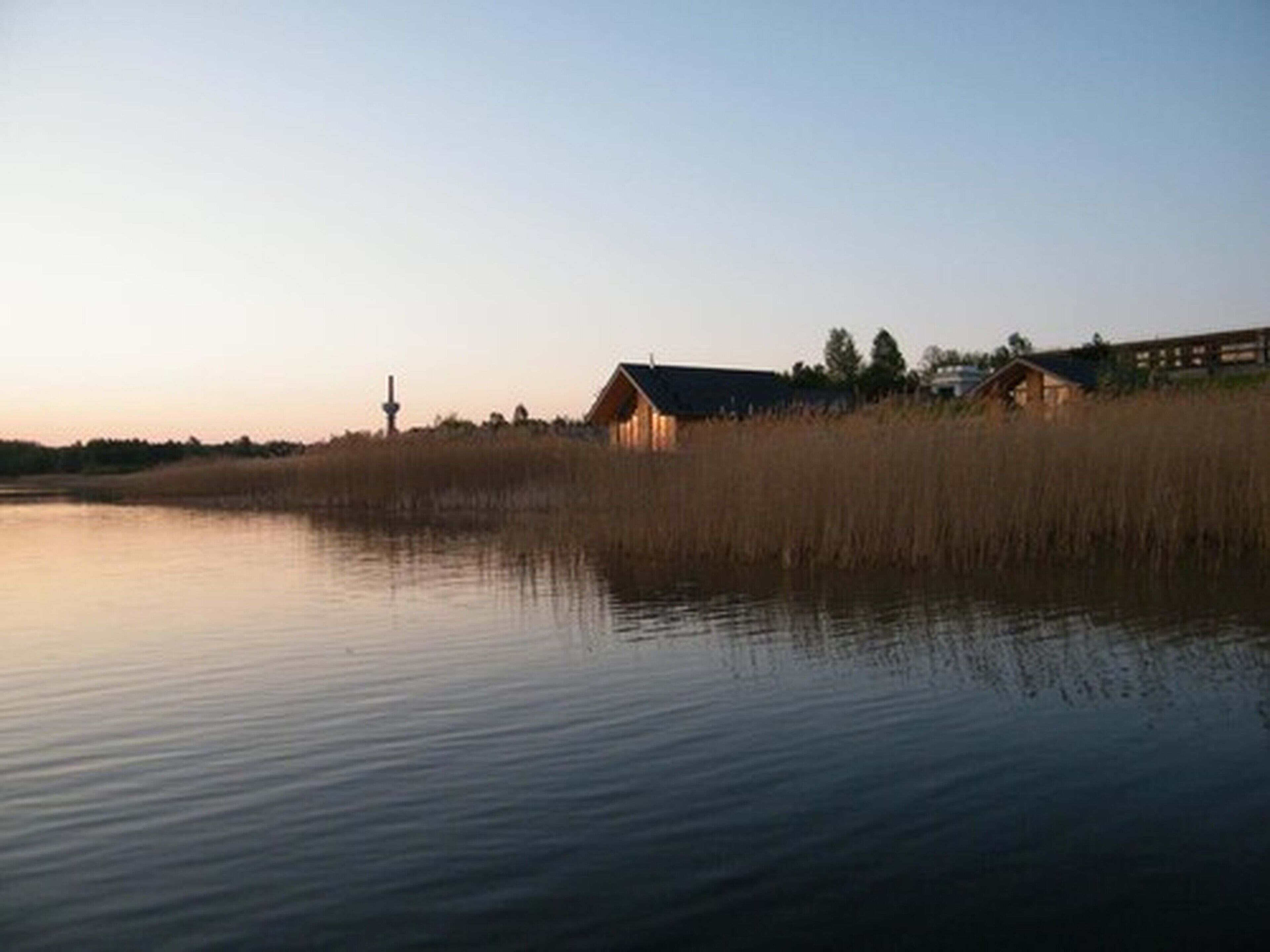 A calm lake with a wooden cabin and a lighthouse in the background.