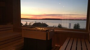 A sauna room with a wooden bench and a wooden box, overlooking a body of water with a sunset view. - See- und Waldresort Gröbern (Muldestausee)