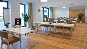 Une salle de conférence équipée de plusieurs tables et chaises, d’un tableau blanc et de plantes en pot.
