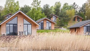A row of modern cabins with large windows, situated near a body of water with tall grasses. - See- und Waldresort Gröbern (Muldestausee)