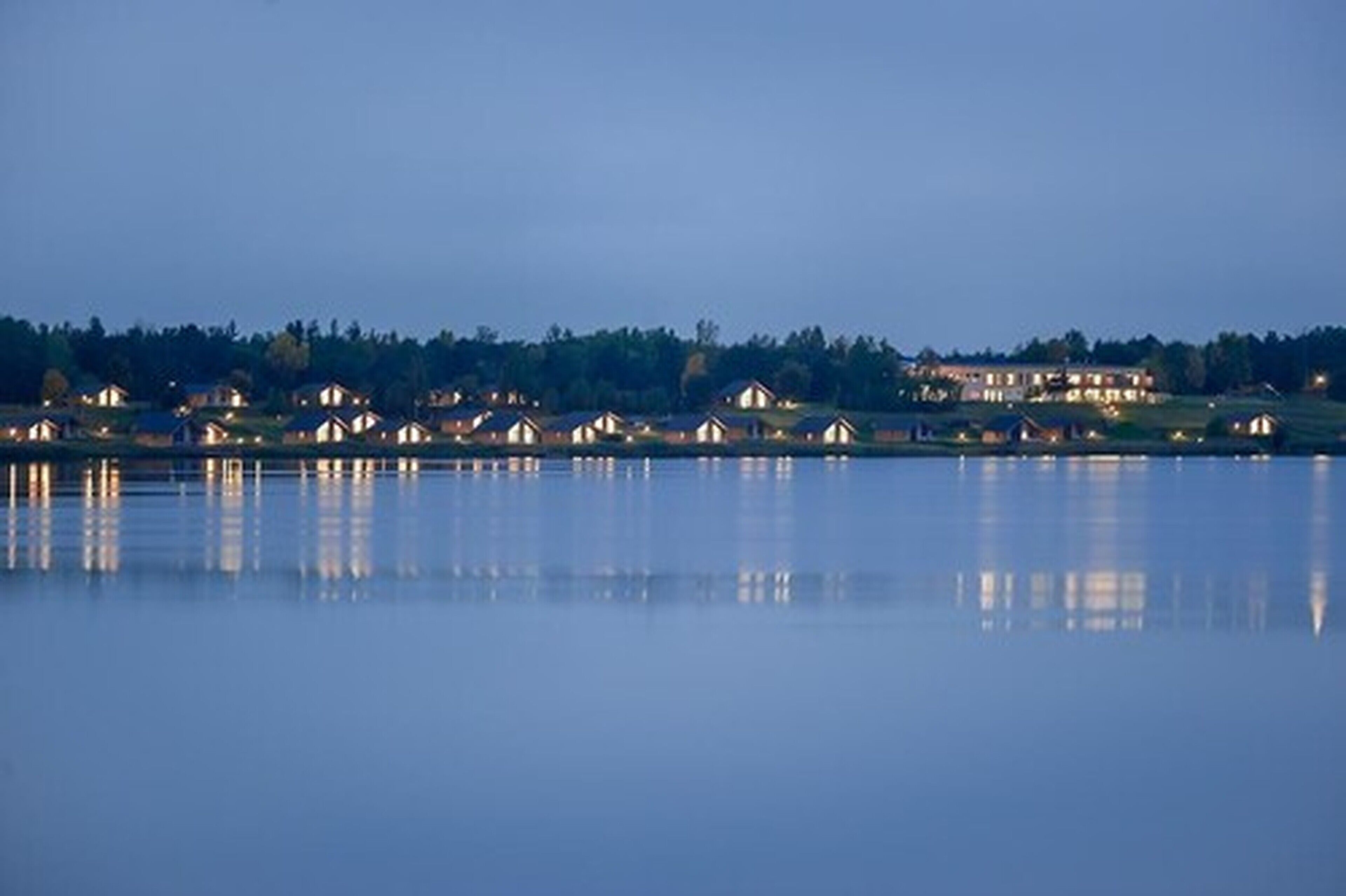 Ein Seeblick auf eine Reihe von Hütten, wobei sich Lichter im Wasser spiegeln.