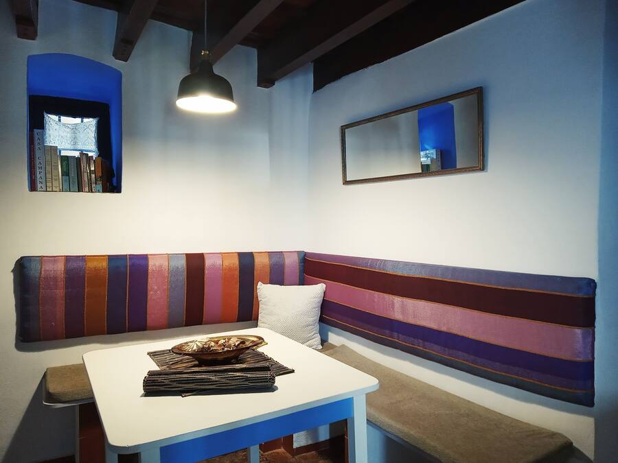 Une pièce avec un banc à rayures, une table sur laquelle se trouve un bol, une lampe suspendue, une bibliothèque et un miroir.