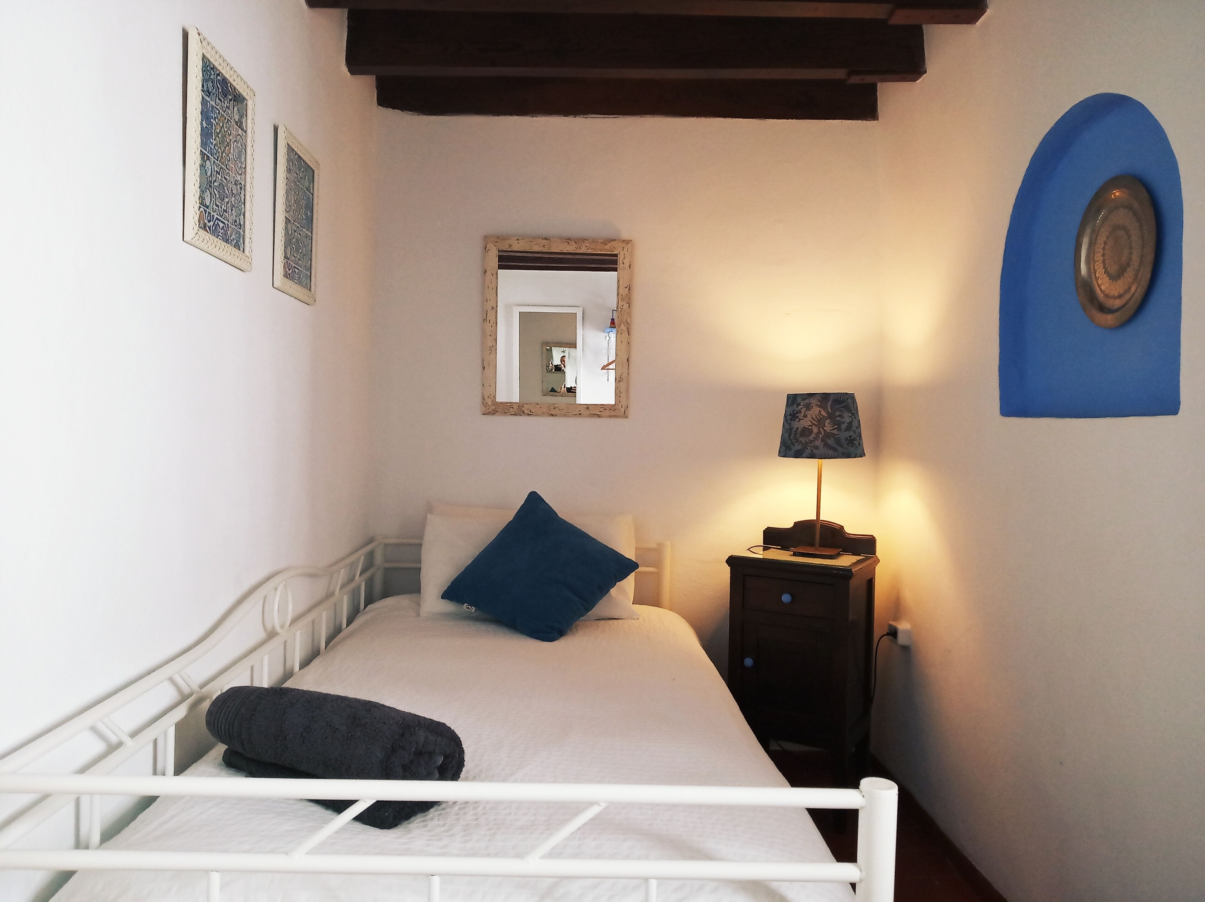 Een slaapkamer met een bed, een nachtkastje met een lamp, een spiegel en twee ingelijste foto’s aan de muur.